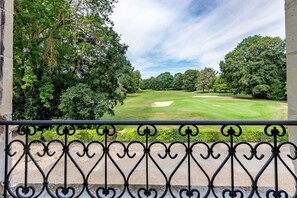 A balcony with wrought iron railing overlooking a golf course with trees and a clear sky.