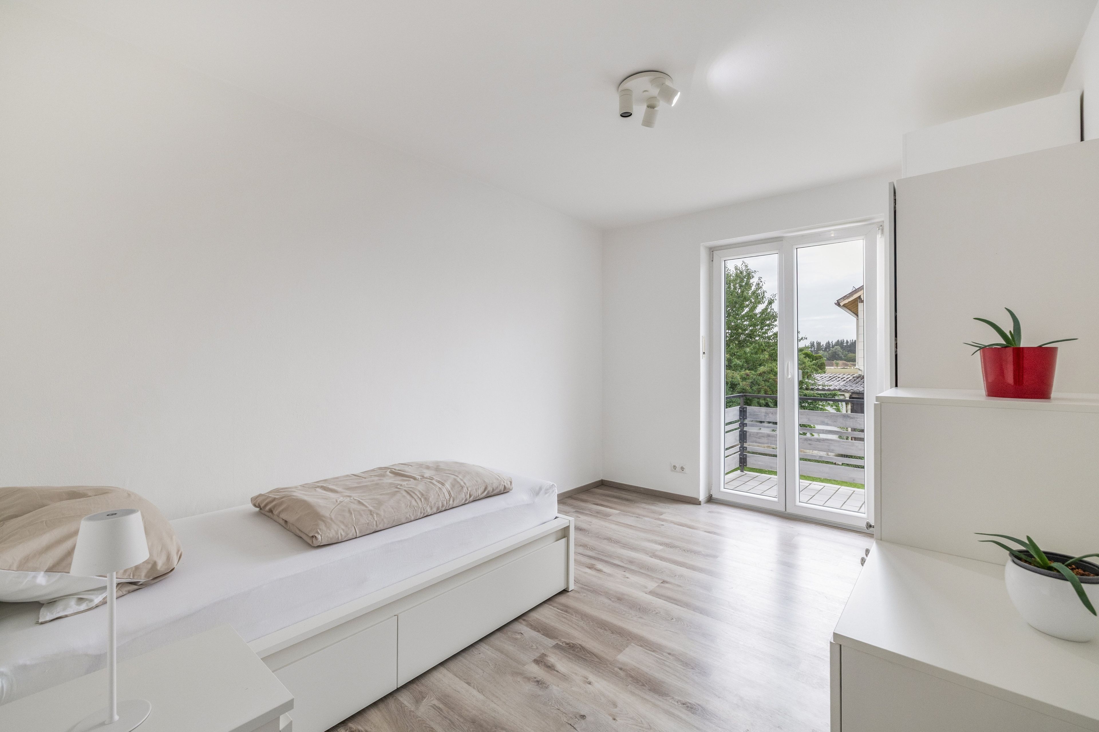 Et minimalistisk soveværelse med seng, natbord og udsigt gennem en skydedør til en udendørs altan.