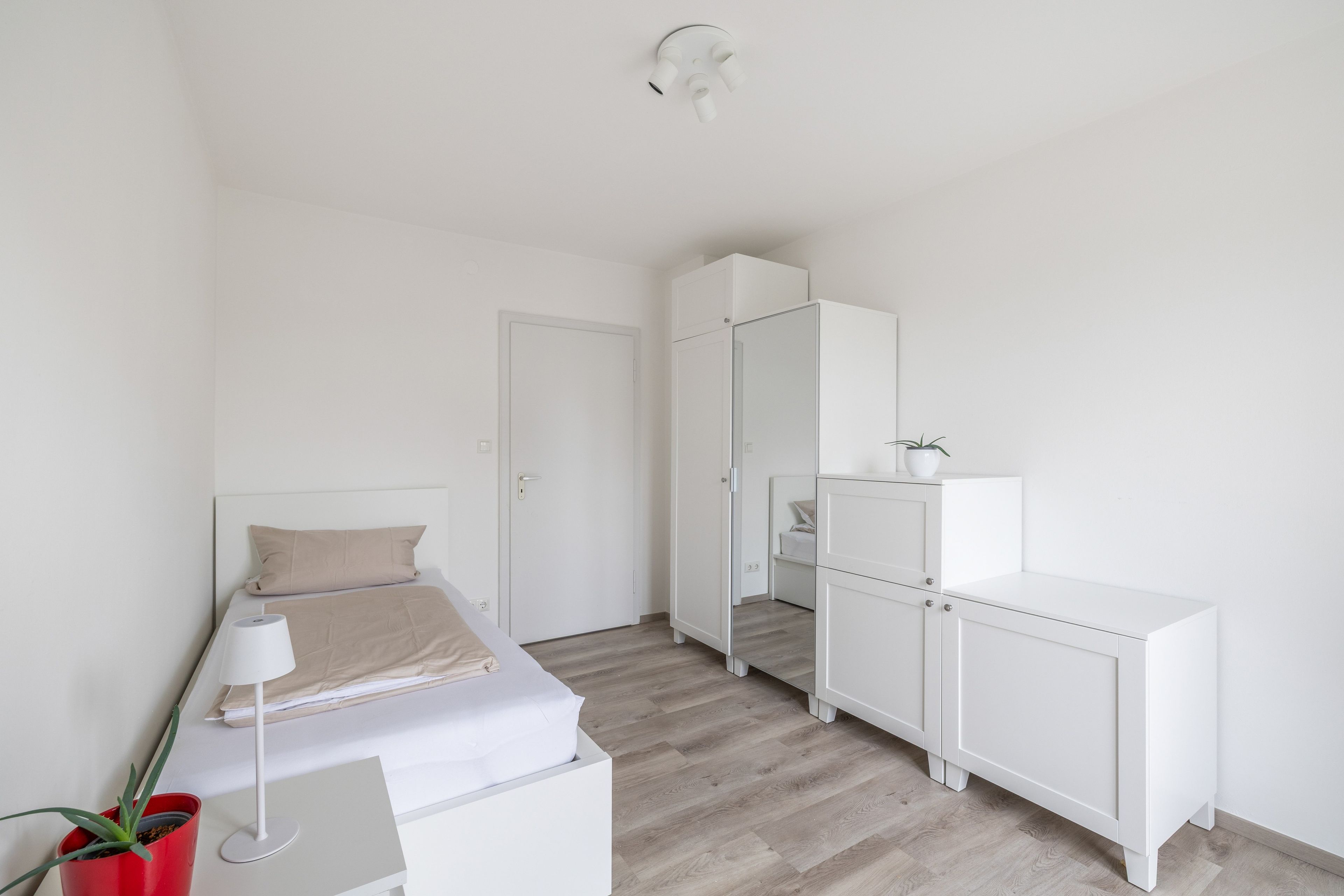 Ein schlicht eingerichtetes Schlafzimmer mit Bett, Nachttisch, Lampe und Kleiderschrank.
