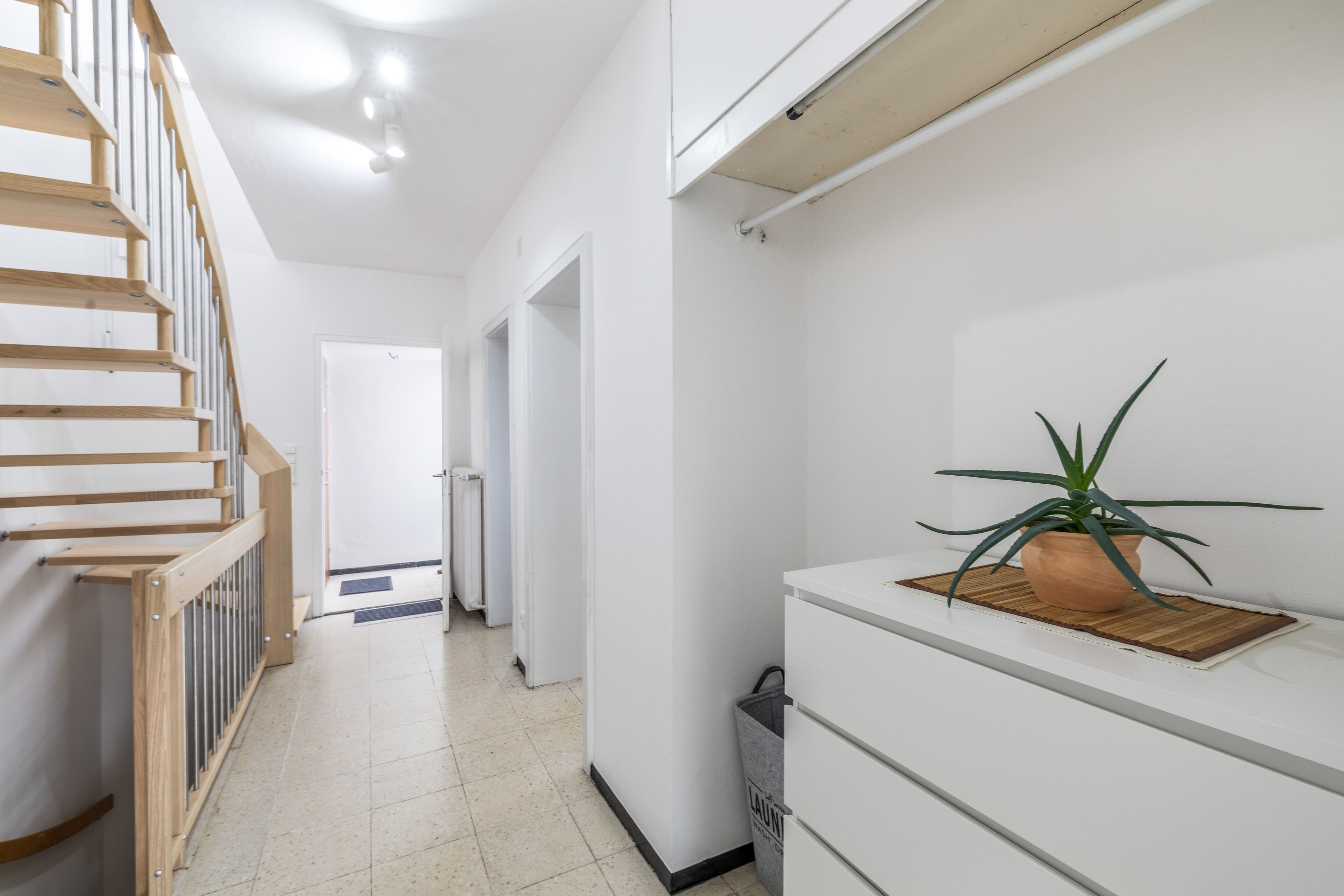 Ein Flur mit einer Holztreppe, einem weißen Schrank mit Schubladen und einer Topfpflanze darauf.