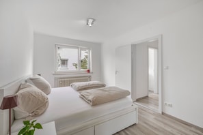 A bedroom with a bed, a window, a radiator, and a door leading to another room. - Holiday Home 'AB12' with Private Terrace, Garden, and Wi-Fi (Oberhaching)