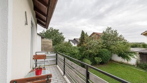 Un balcon avec une table et des chaises, un pot de fleurs et une vue sur un jardin verdoyant et des bâtiments.