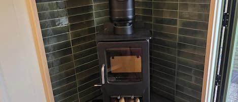 Une pièce d’angle dotée d’un poêle à bois encastré, d’un petit espace de rangement en dessous et offrant une vue à travers une porte vitrée.