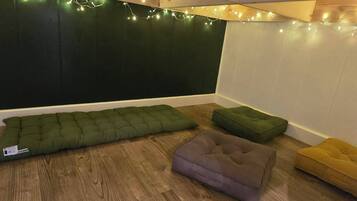 Une pièce chaleureuse avec un banc rembourré vert, un coussin violet et un pouf jaune, le tout posé sur un plancher en bois.