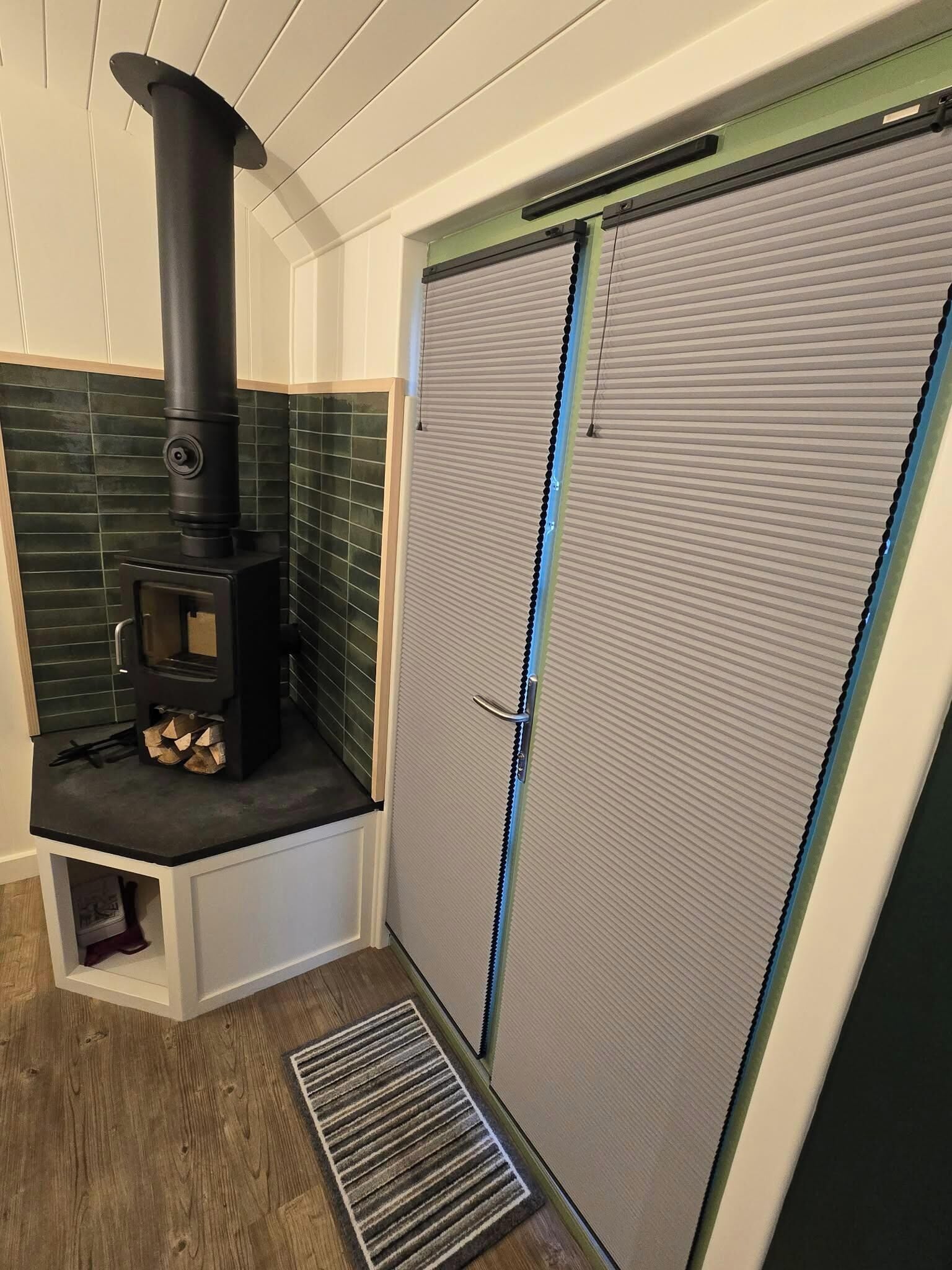 A compact room with a wood-burning stove, a closed door, and a small entryway.