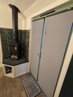 A compact room with a wood-burning stove, a closed door, and a small entryway.