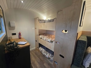 Ett litet rum med våningssängar, ett litet skrivbord med en växt och en brandsläckare.