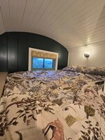 Un dormitorio con techo curvo, una ventana con vista a árboles y una cama con colcha de estampado floral.