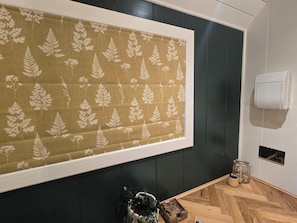 A room with a large patterned curtain, a wooden floor, a wall-mounted air conditioner, and a small plant on the floor.