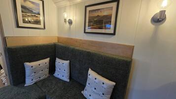 A corner seating area with a dark green upholstered sofa, two pillows with a sheep pattern, and two framed landscape paintings on the wall.