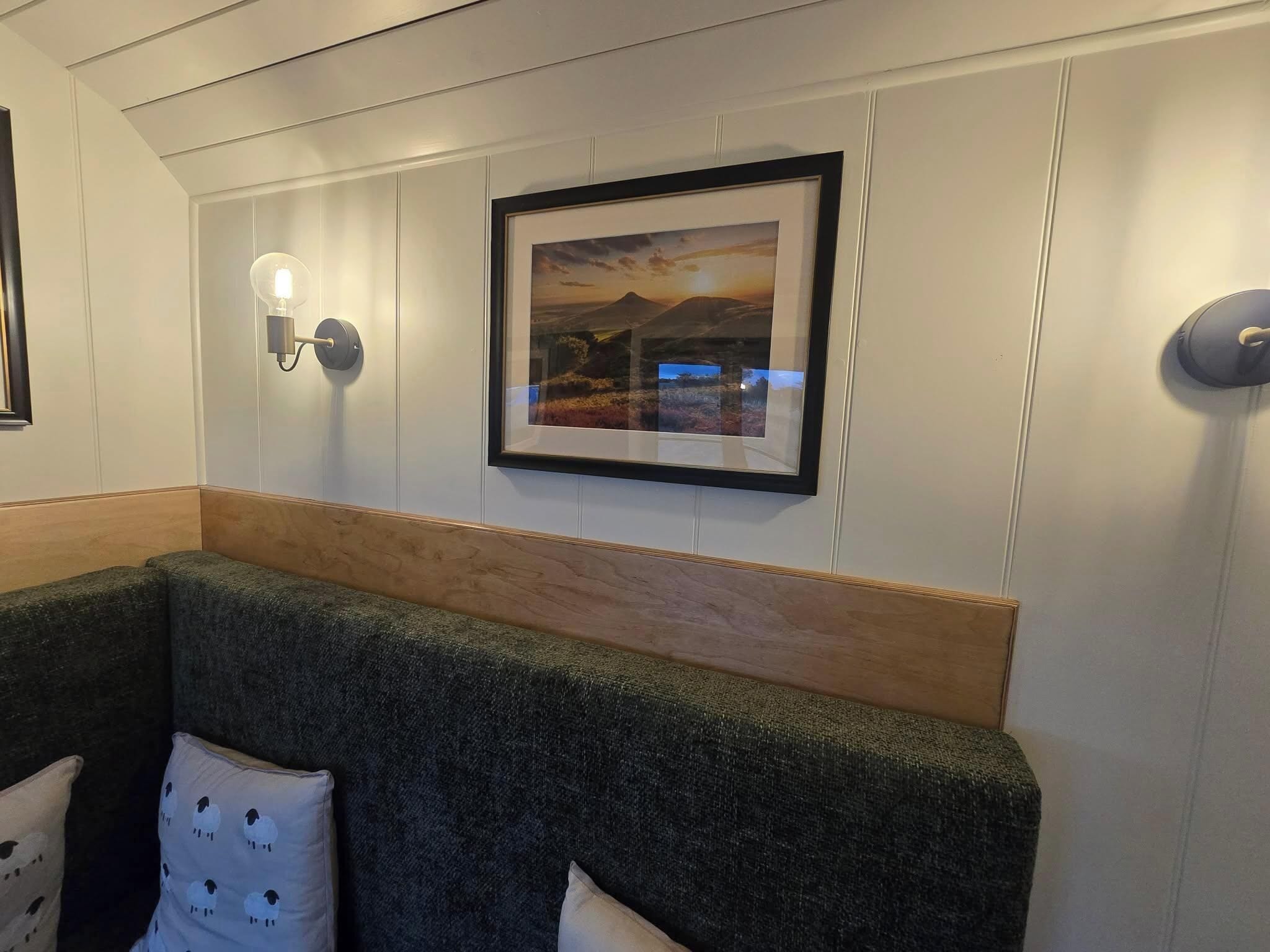A room with a wooden headboard couch, a framed picture on the wall, and a wall-mounted light fixture.