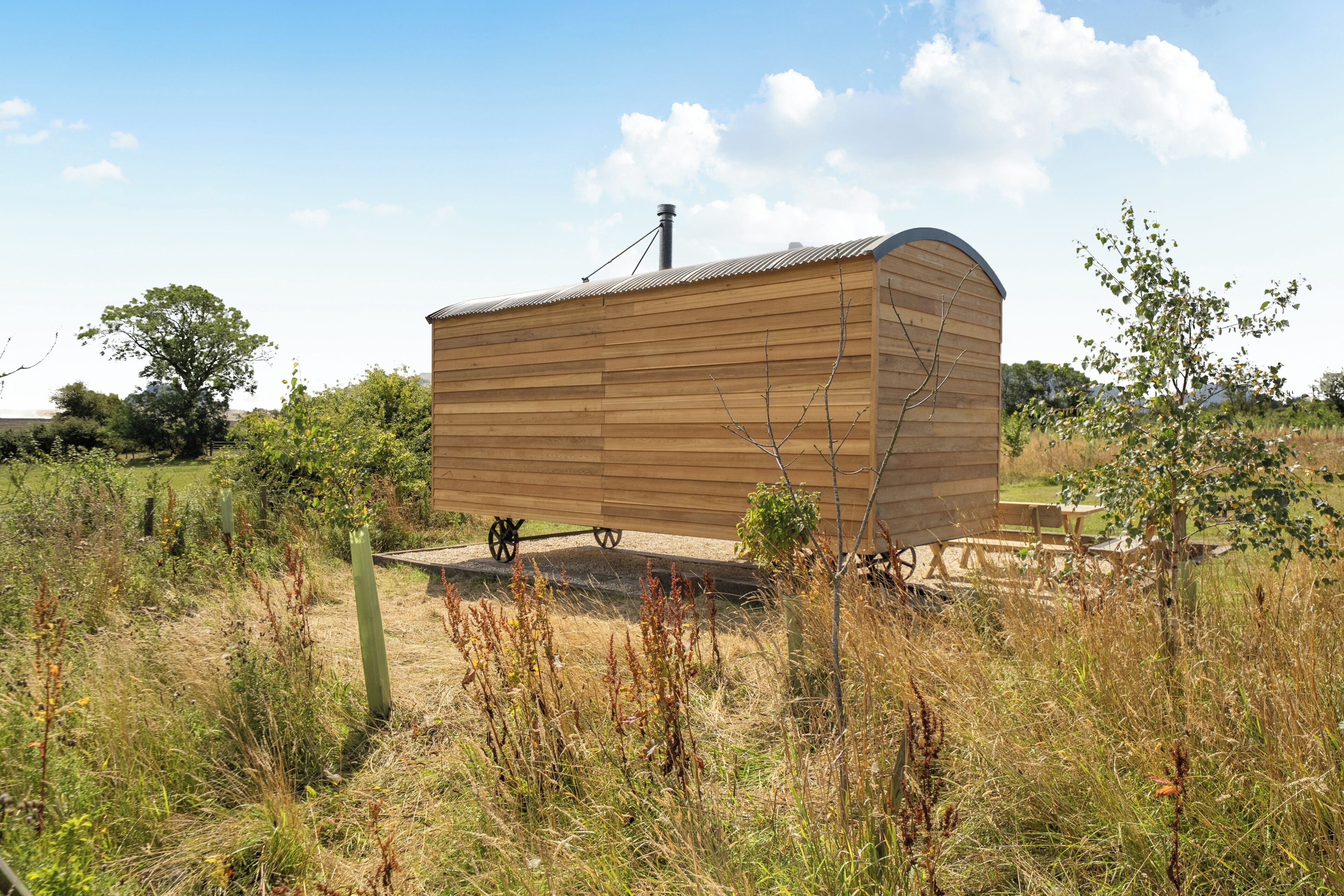 A wooden structure with a curved roof, surrounded by natural vegetation and a clear sky.