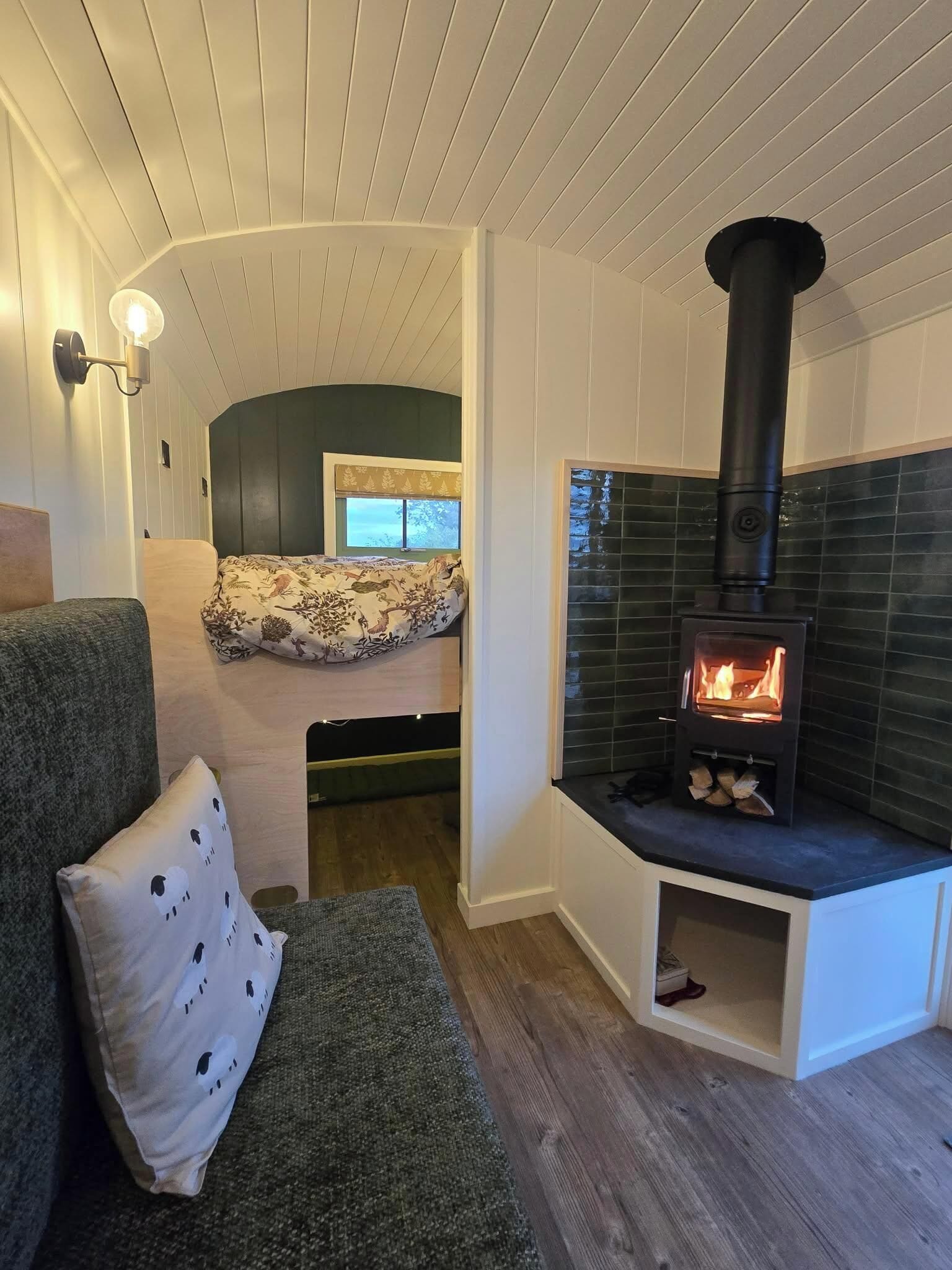 A cozy living room with a built-in wood stove, a sofa with a patterned throw, and a window with a view.