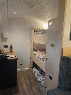 A bunk bed with a wooden headboard, a desk with a plant, and a fire extinguisher.