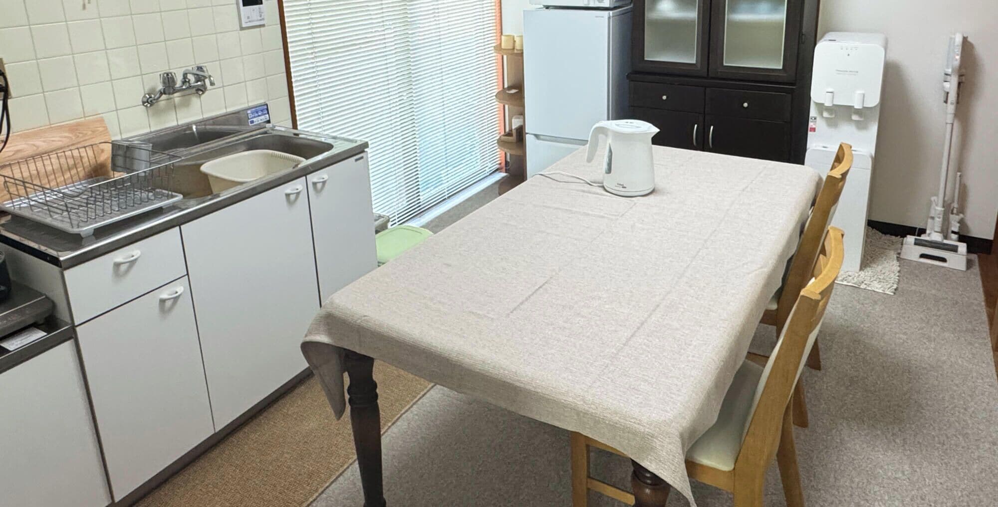 A kitchen with a table, chairs, a sink, cabinets, and a water dispenser.