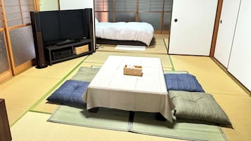 Et traditionelt japansk rum med tatamimåtter, et lavt bord med en kasse, en seng med hvidt sengetøj og et fjernsyn på et stativ.