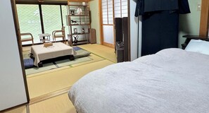 Una habitación japonesa tradicional con suelo de tatami, un futón, una pequeña mesa con una silla y una estantería con objetos decorativos.