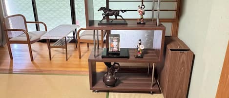 Una habitación tradicional japonesa con suelo de tatami, una mesa de madera baja, una silla y un estante con objetos decorativos.