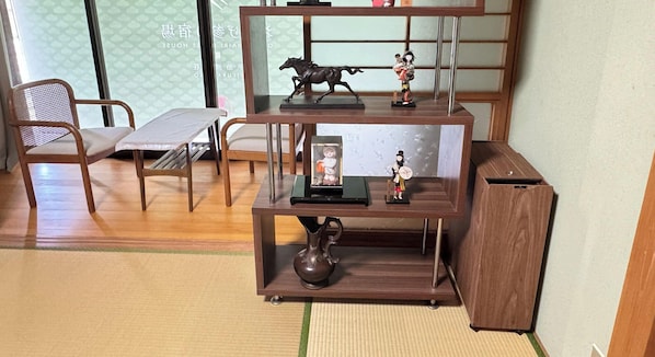 Una habitación tradicional japonesa con suelo de tatami, una mesa de madera baja, una silla y un estante con objetos decorativos.