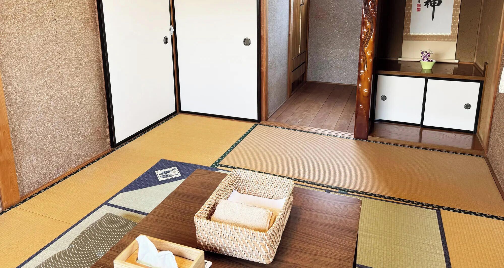 A traditional Japanese room with tatami flooring, a low wooden table, and a woven basket with a towel.