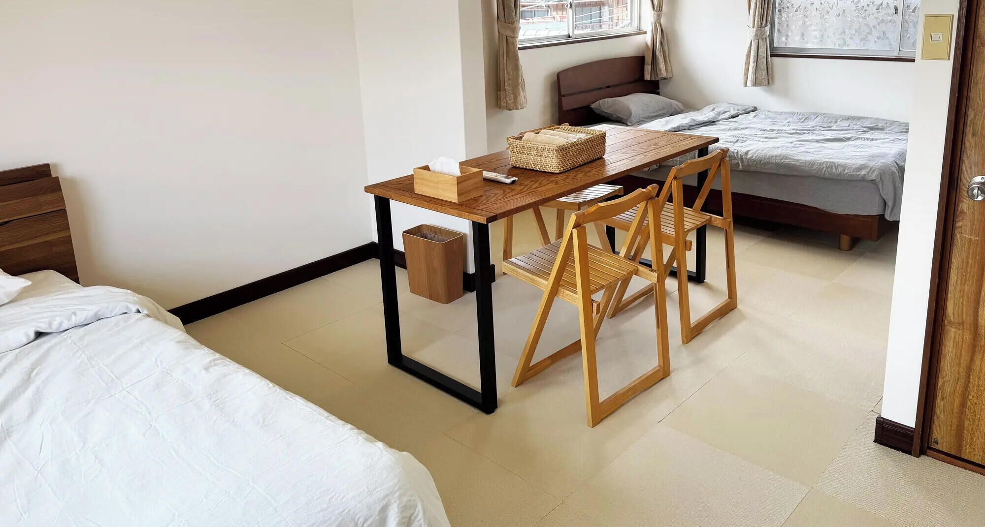 A compact hotel room with a bed, a small desk with a chair, a bedside table, and a window with curtains.