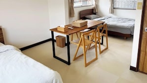 Quarto de hotel pequeno com cama, uma secretária, uma cadeira, mesa de cabeceira e janela com cortinas.