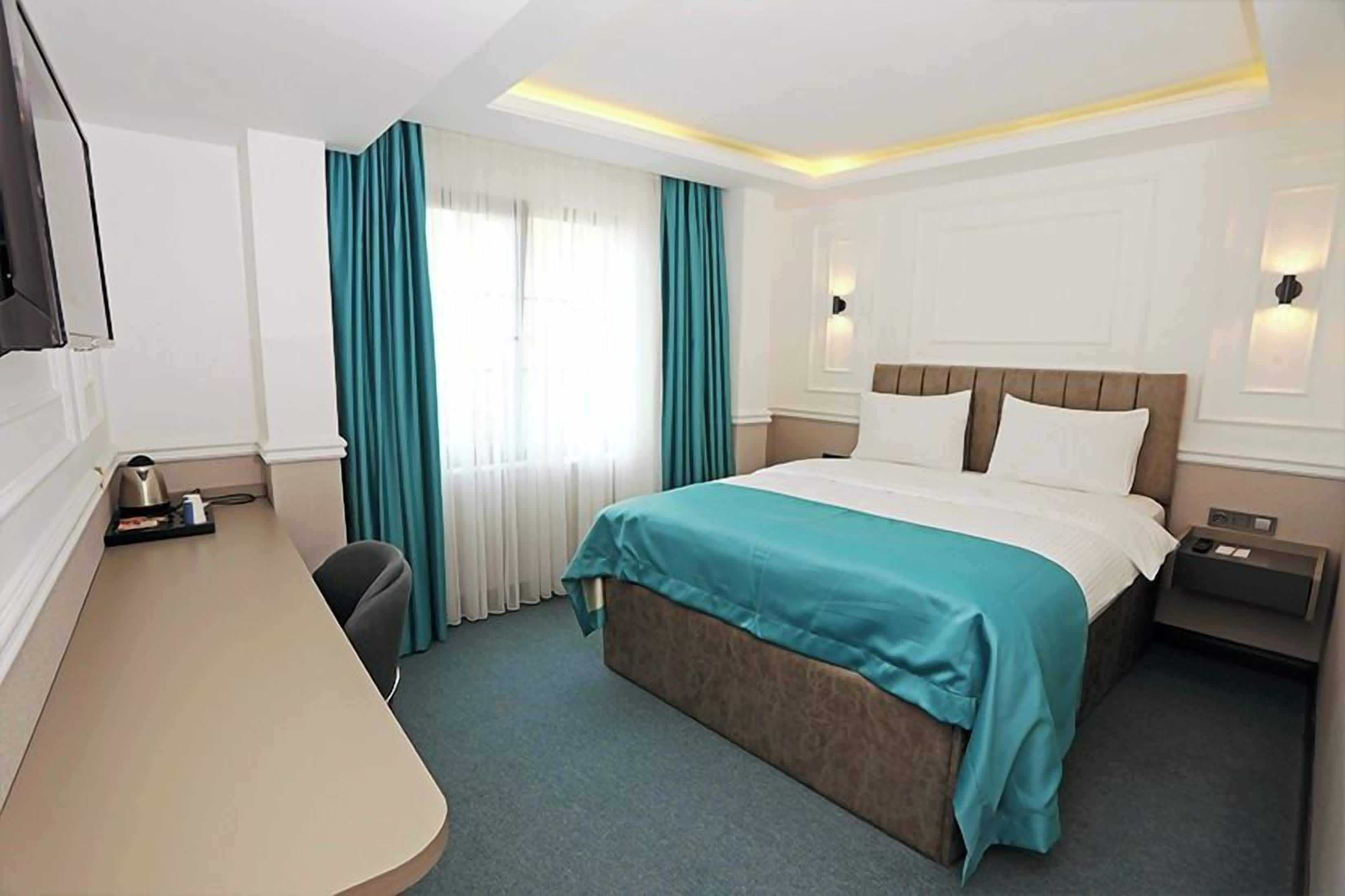 A hotel room with a bed, a desk, a chair, a nightstand, and a TV.