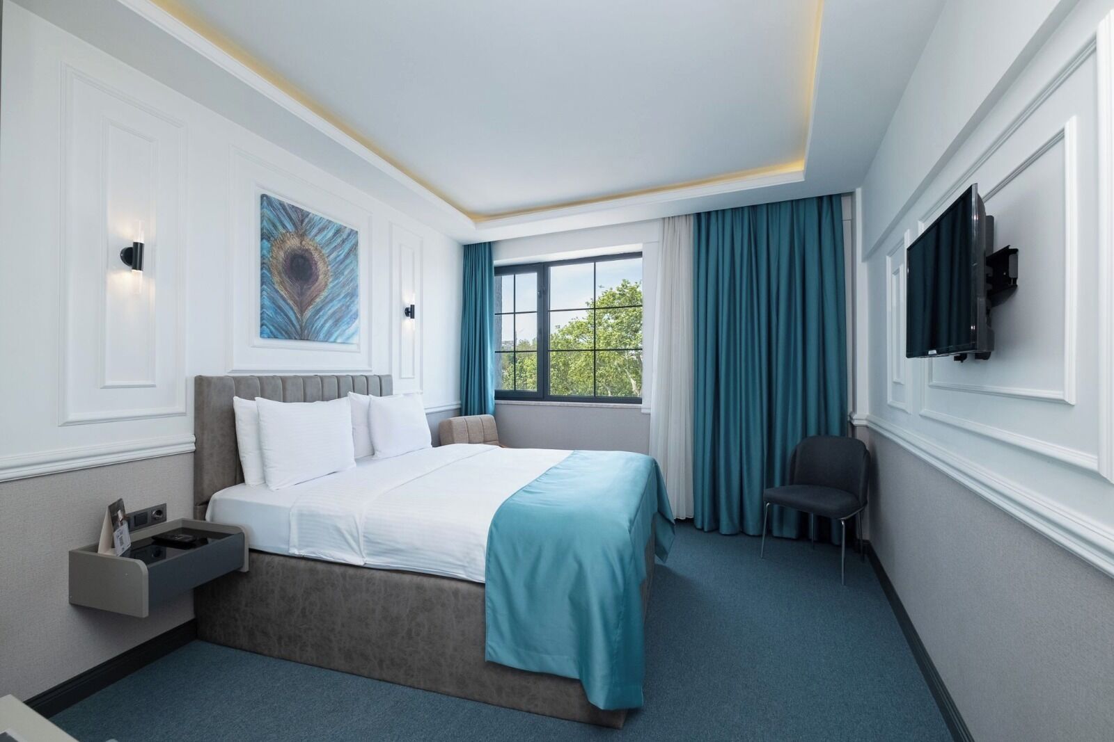A hotel room with a bed, a desk, a chair, a TV, and a window with curtains.