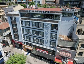 Un hotel de varios pisos con un llamativo letrero 'May Hotel', un restaurante McDonald's y un 'Café Balik' en la planta baja.