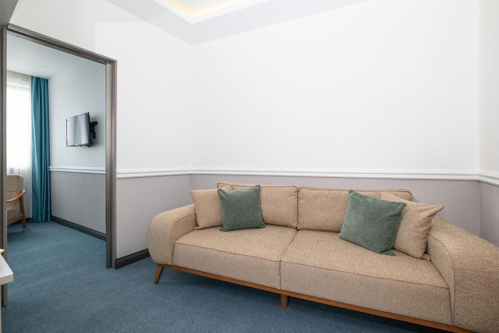 A room with a beige sofa, two green pillows, a wooden floor, and a blue carpet.