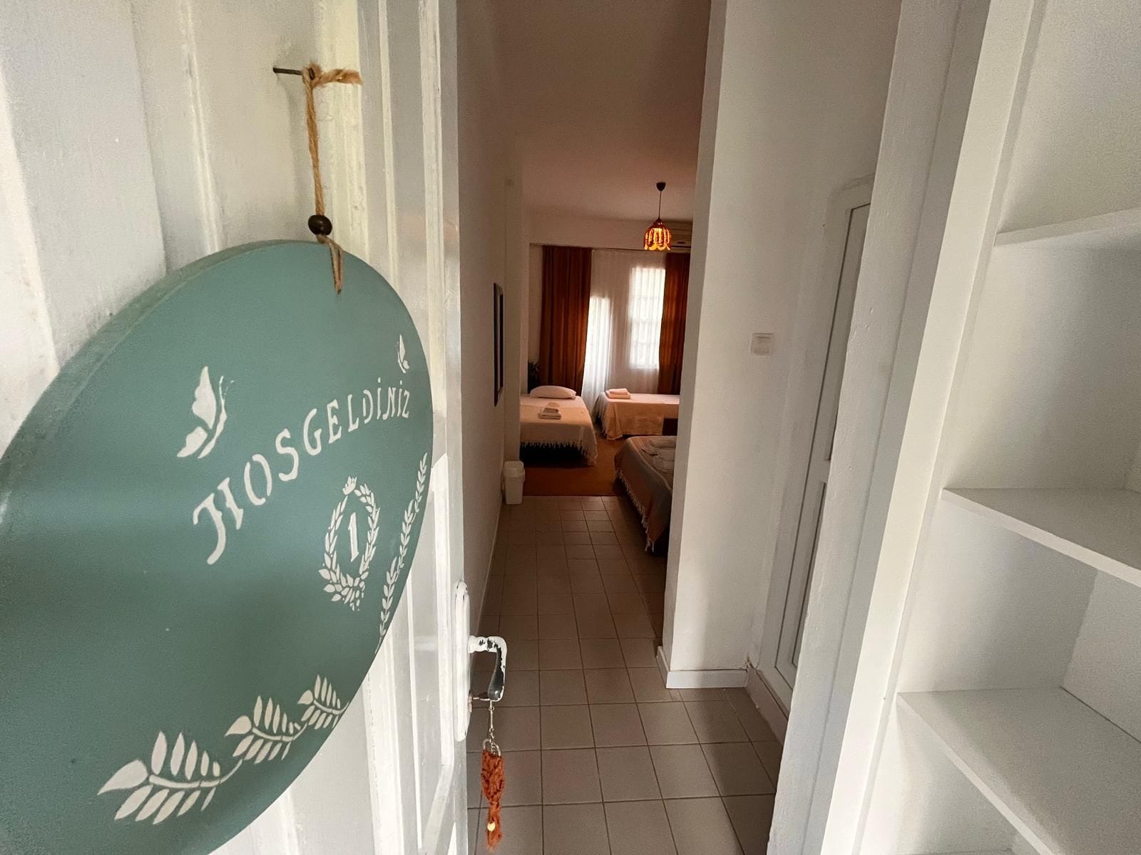 A hallway leading to a bedroom with a bed, a hanging light fixture, and a towel rack.