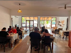 A dining area with tables and chairs, large windows, and a ceiling fan.