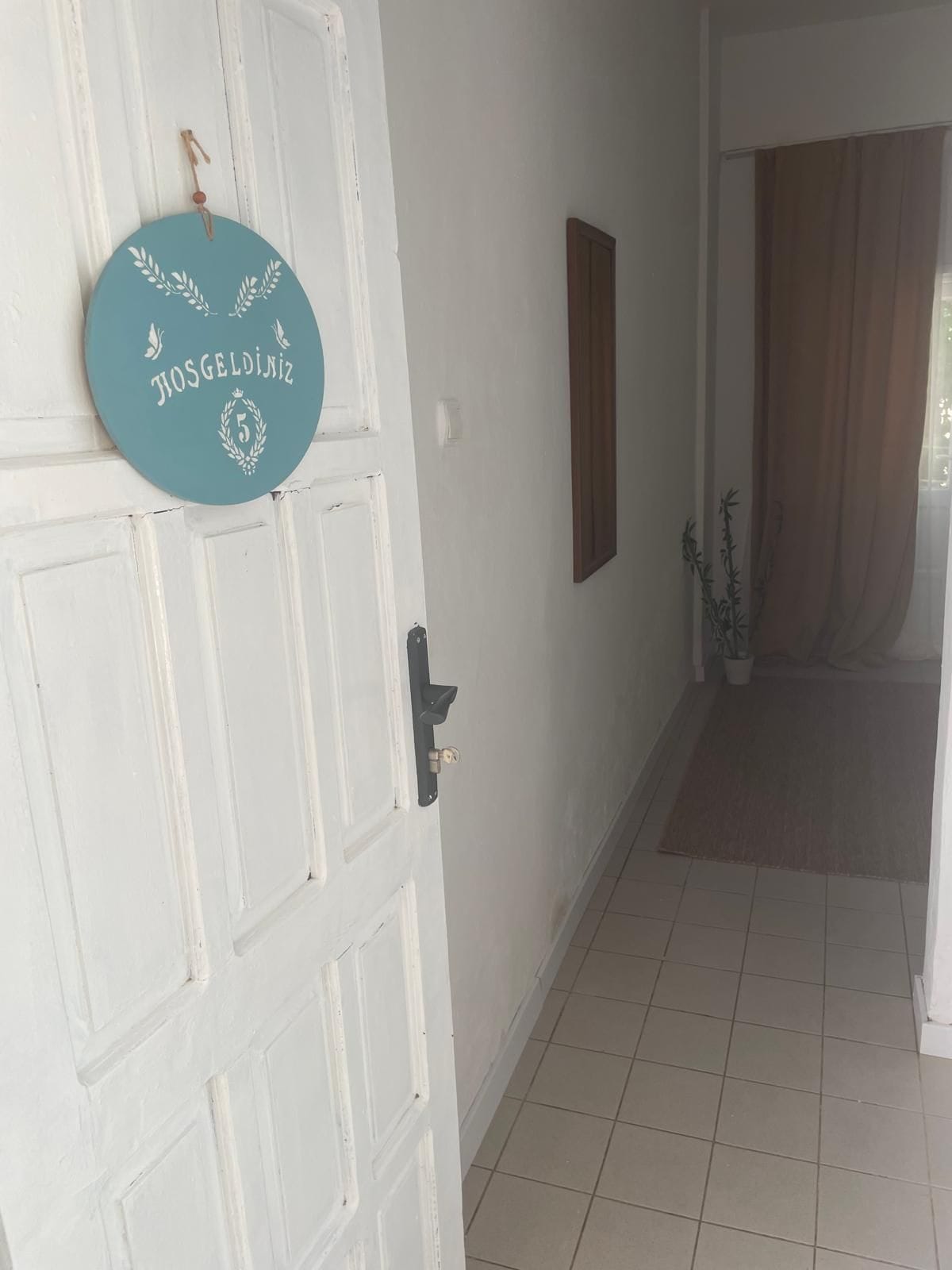 A white door with a teal plaque, a wooden door frame, a tiled floor, and a brown curtain.