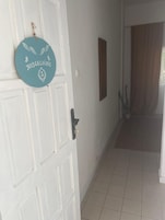 Una puerta blanca con una placa azul verdosa, un marco de madera, piso de baldosas y una cortina marrón.