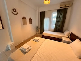 Una habitación de hotel con una cama, una mesita de noche, un aire acondicionado instalado en la pared y una pequeña planta en maceta.