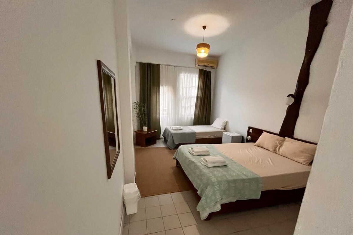 A hotel room with a bed, bedside tables, a mirror, a window with curtains, and a ceiling light.