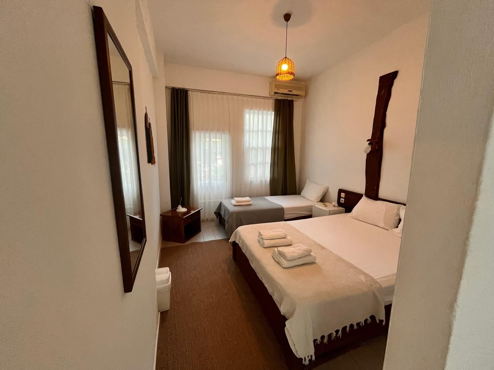 Een hotelkamer met een bed, nachtkastjes, een spiegel, een airconditioning en een hanglamp.