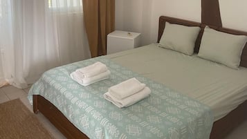 Een hotelkamer met een bed, nachtkastje, airconditioning en een raam met gordijnen.