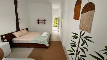 Habitación de hotel con cama, mesita de noche, una silla, una planta y vistas al exterior.