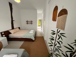 Habitación de hotel con cama, mesita de noche, una silla, una planta y vistas al exterior.