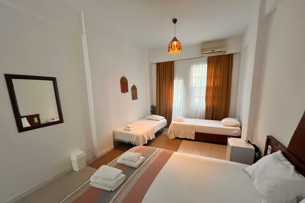 A hotel room with a large bed, two smaller beds, a mirror, and a hanging light fixture.