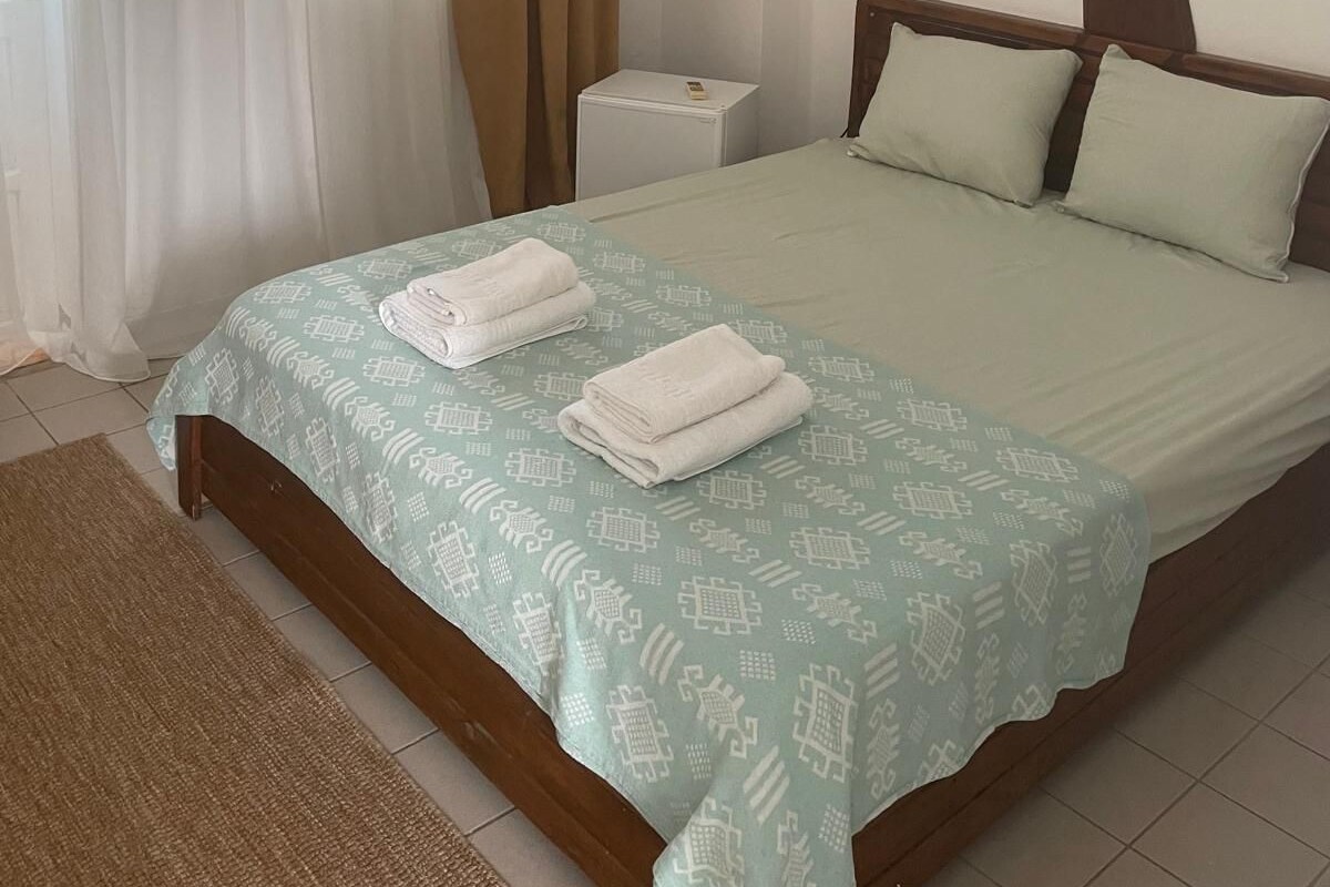 A hotel room with a bed, a bedside table, an air conditioning unit, and a window with curtains.