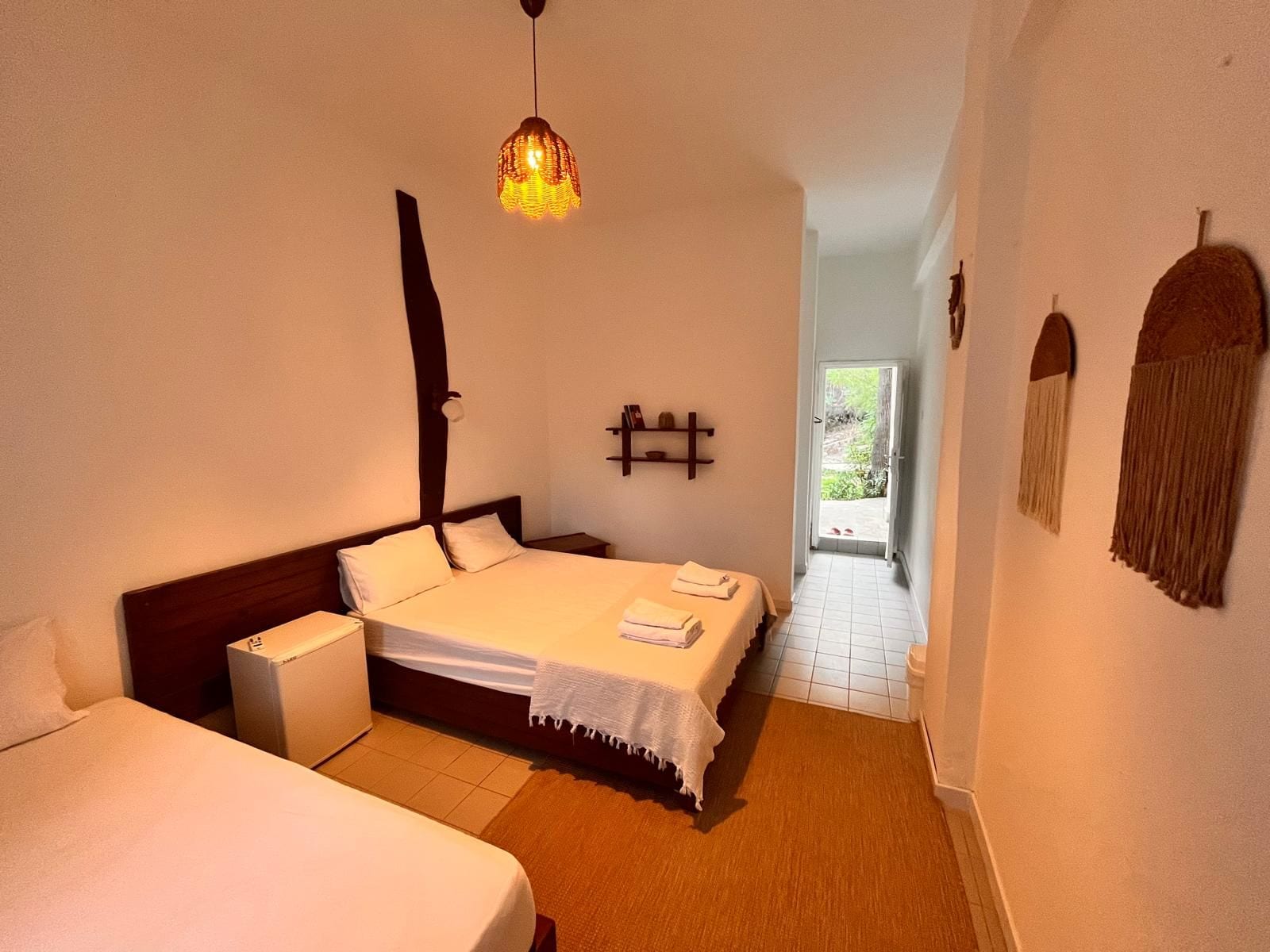 A hotel room with a bed, bedside tables, a hanging light fixture, and a view of the outdoors.