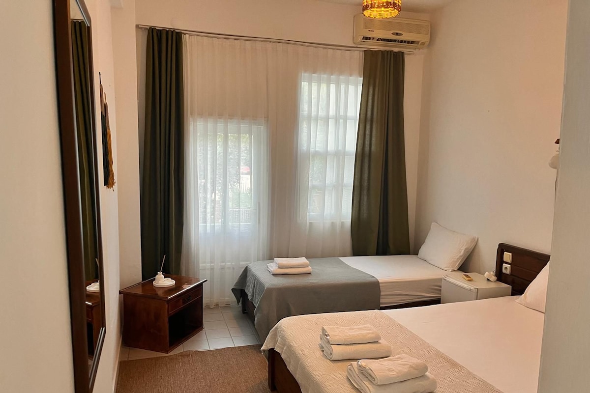 A hotel room with two beds, a bedside table, a nightstand, and a window with curtains.