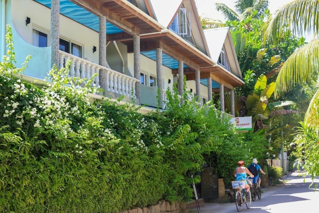 A hotel with a balcony, lush greenery, and a sign indicating it is a resident hotel.