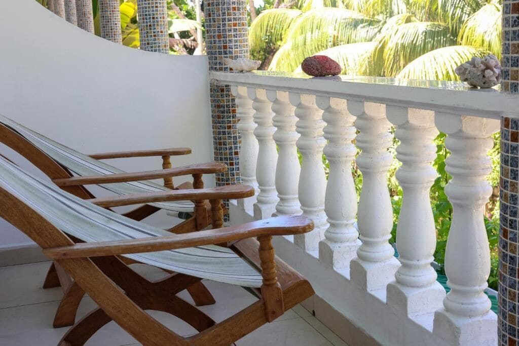 A balcony with a white balustrade, a hammock, and a view of palm trees.