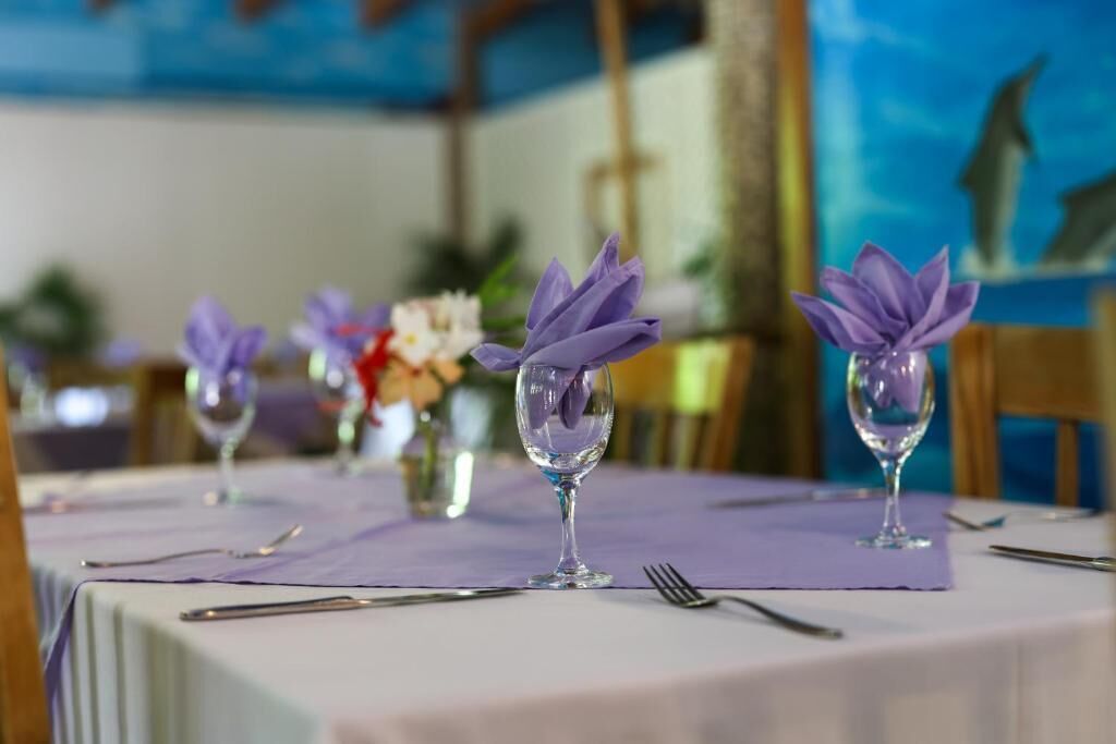 A dining table with a purple tablecloth, clear glassware, and purple napkins.