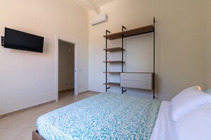 Una camera da letto con un letto, una TV a parete, un armadio con scaffali e una porta che dà su un'altra stanza.