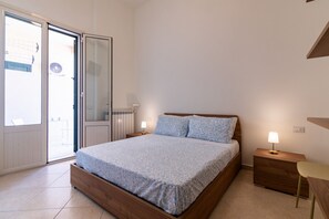 Een slaapkamer met een bed, nachtkastjes, een stoel en een glazen schuifdeur die leidt naar een buitenruimte.