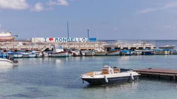 Een jachthaven met aangemeerde boten, een groot gebouw met de tekst 'I ♥ MONDELLO', en een heldere lucht.